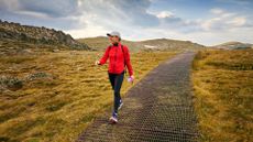 Woman walking down path as part of weekend exercise, wearing leggings and coat with hat