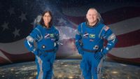 two astronauts pose for a portrait in blue spacesuits