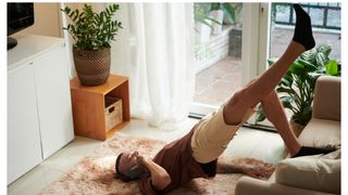 Pelvic floor exercises: Man performing a single leg glute bridge against his sofa in his living room