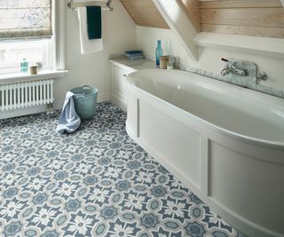 blue and white patterned vinyl floor in room with white bath and sloped ceiling