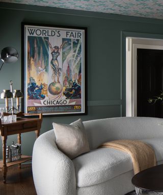 A green room with a white curved sofa, a vintage bar cart, and a vintage poster advertising the Chicago World's Fair