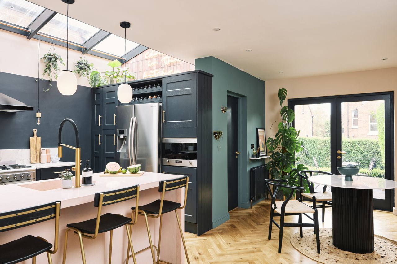 Kitchen-diner with parquet flooring, blue wall and kitchen units, pink island, and black and marble dining set