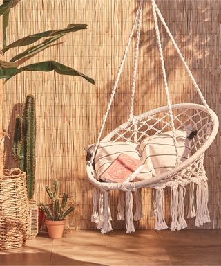 A woven macramé swing chair seat in backyard with outdoor cushions and plants