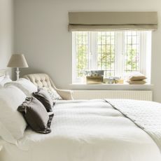 Cream bedroom with white bedding, a window and two lampshades either side of bed.