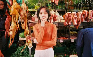 woman smoking in front of hanging meats