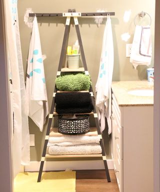 Freestanding pyramid style bathroom shelving with towels, and baskets and container in small bathroom with green bath mat