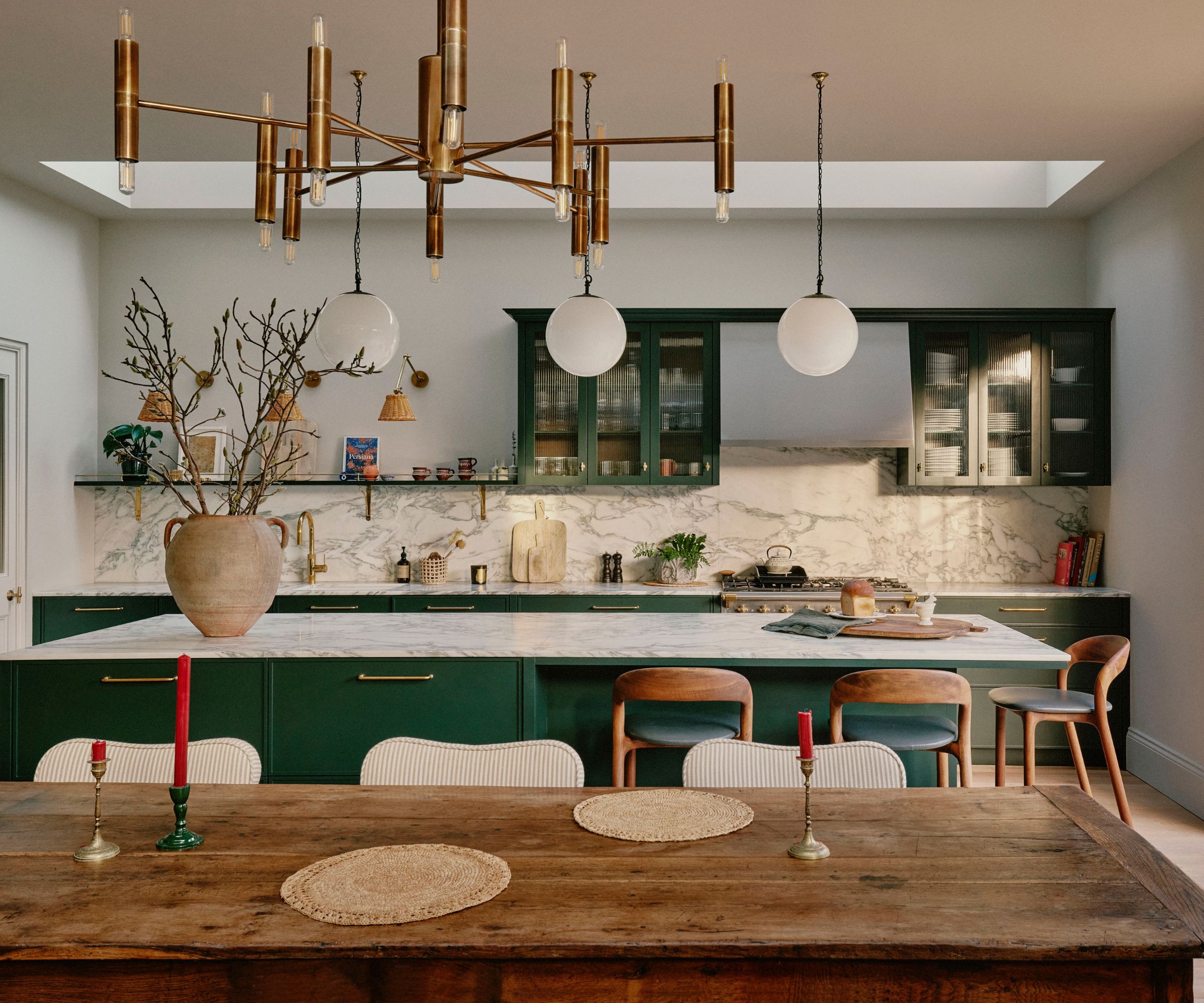 A transitional kitchen with white walls, green cabinets, marble countertops, and a large wood dining table