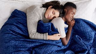 Two women sleep underneath a blue Gravity Weighted Blanket