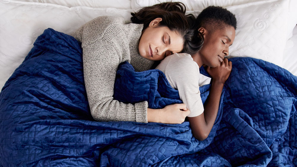 Two women sleep underneath a blue Gravity Weighted Blanket