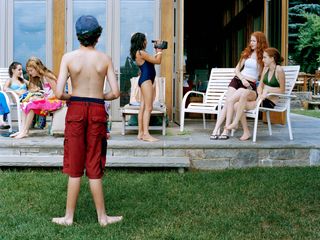 An outdoor gathering of young teenage children, one is recording two others with a camcorder