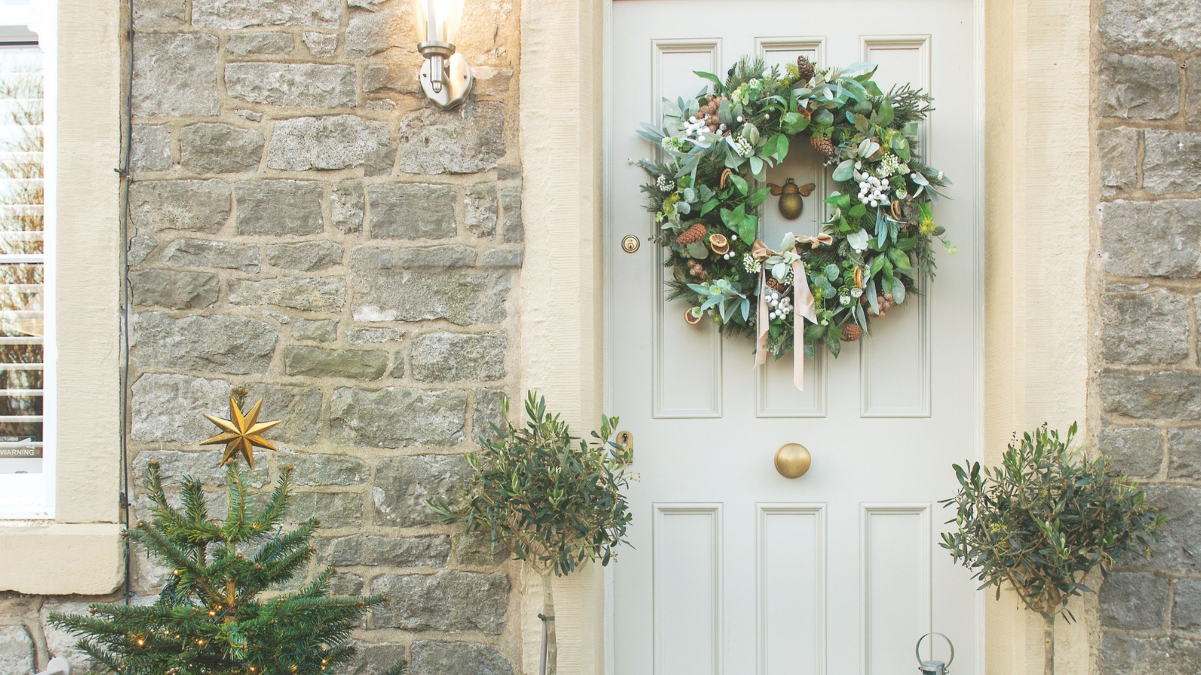 Small christmas tree, two potted trees and festive wreath on a grey door.