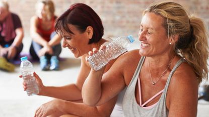 Two women laughing and drinking from water bottle after workout class