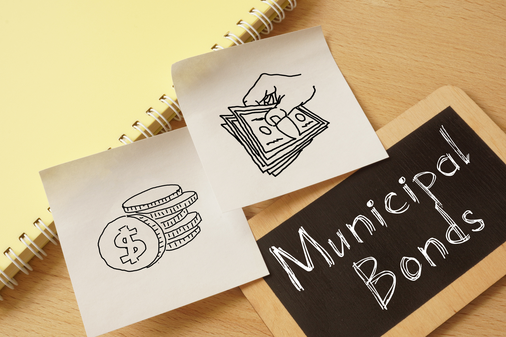 Municipal bonds written on a chalkboard next to rough drawings of a hand holding money and a stack of coins