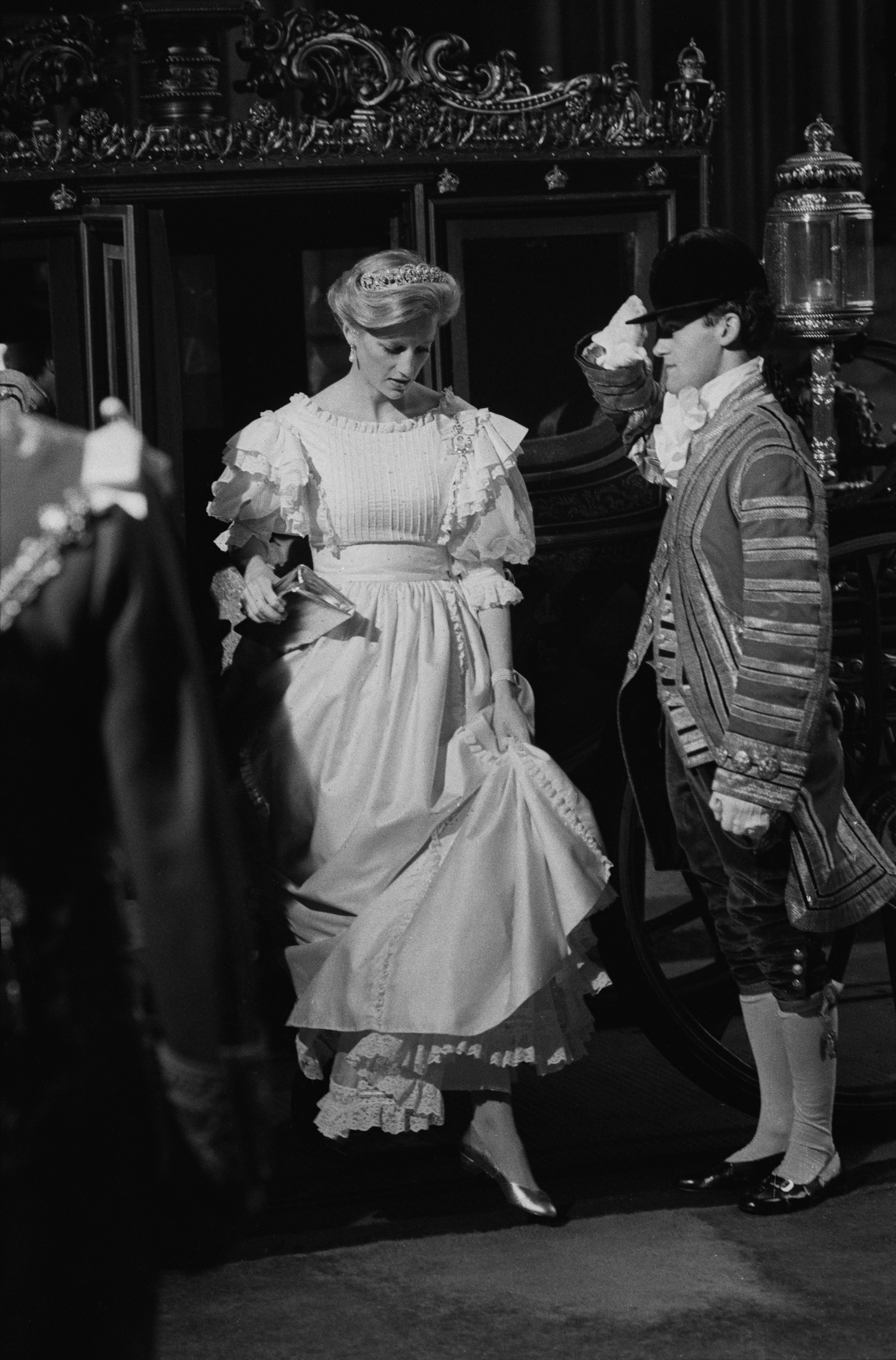 Princess Diana wearing a long white dress stepping out of a carriage and lifting her hem