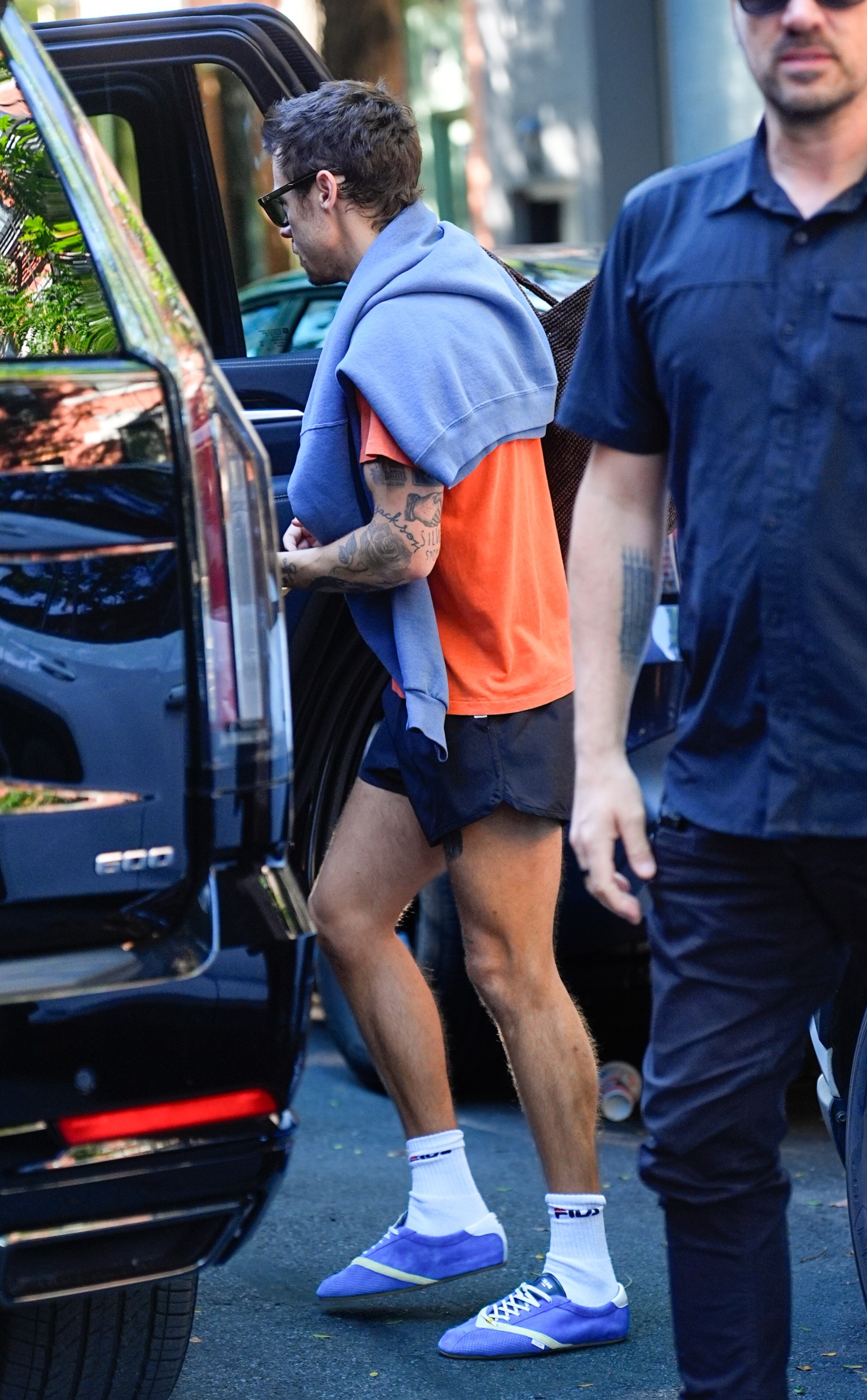 An image of Harry Styles wearing an orange t-shirt with track shorts and Celine Flat Sneakers whilst in New York.