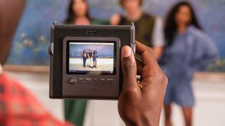 Instax Wide Evo instant camera being used to take a group shot of three people