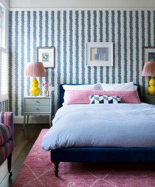 Bedroom ideas for teenagers featuring a blue and white patterned wallpaper and furnishings with a pink rug and yellow bedside lamps.