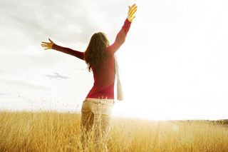 A woman raises her arm to greet the sun with joy.