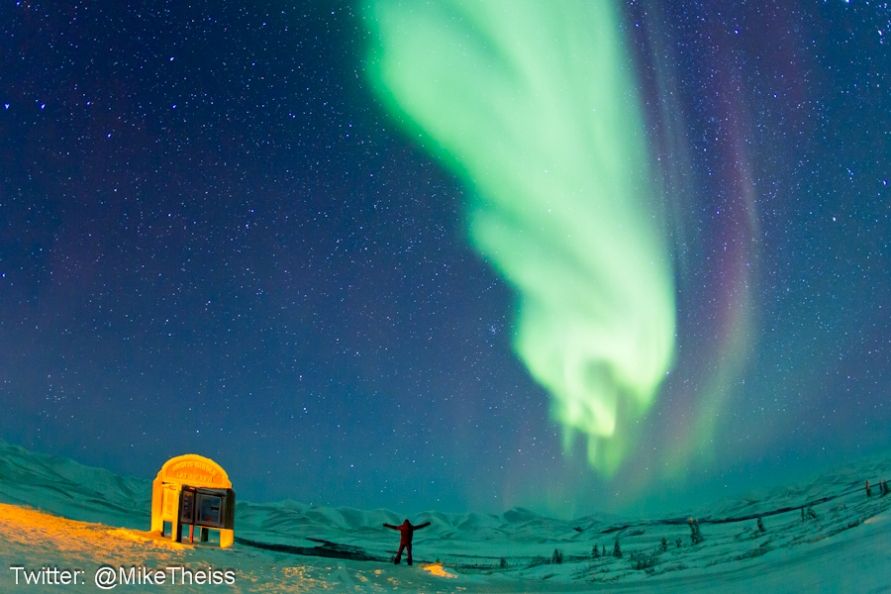 National Geographic photographer Mike Theiss taking in the northern lights. The sign marks the edge of the Arctic Circle can be seen to the left. 