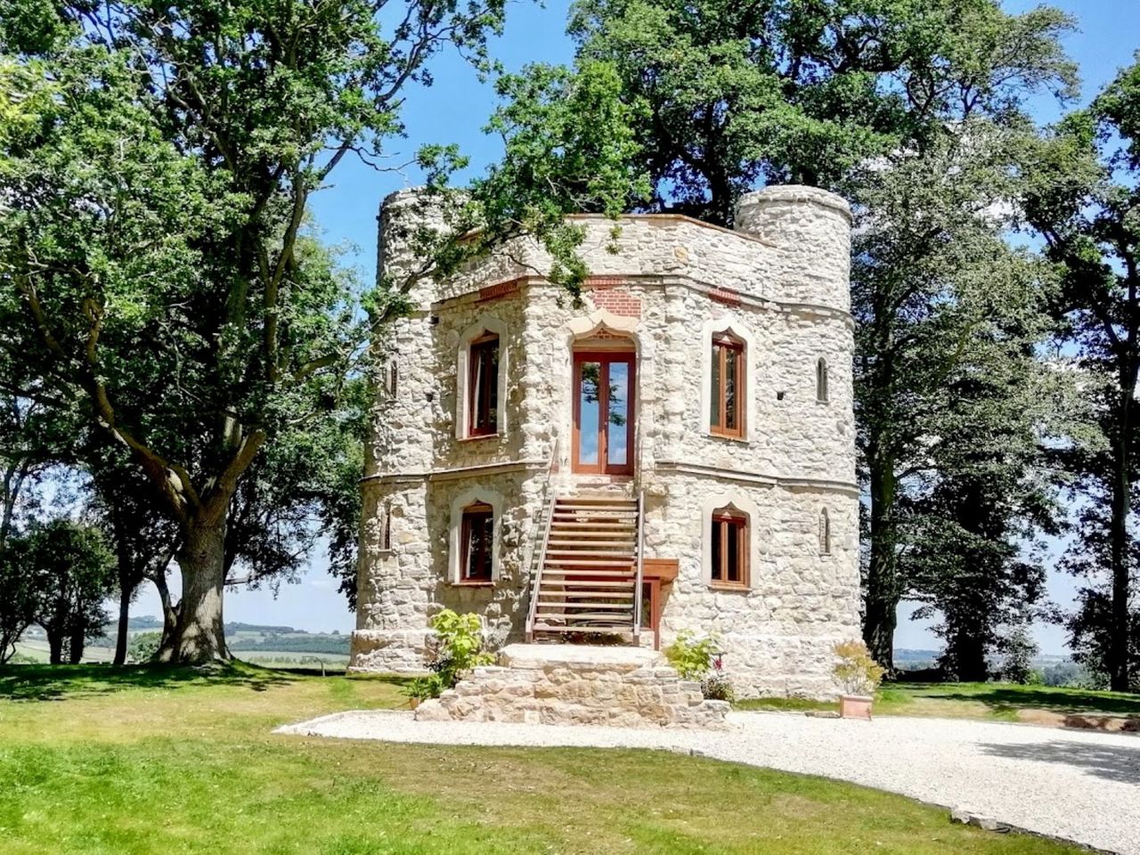 Dinton Castle with bright white brickwork in a front on shot in the sun which is surrounded by trees