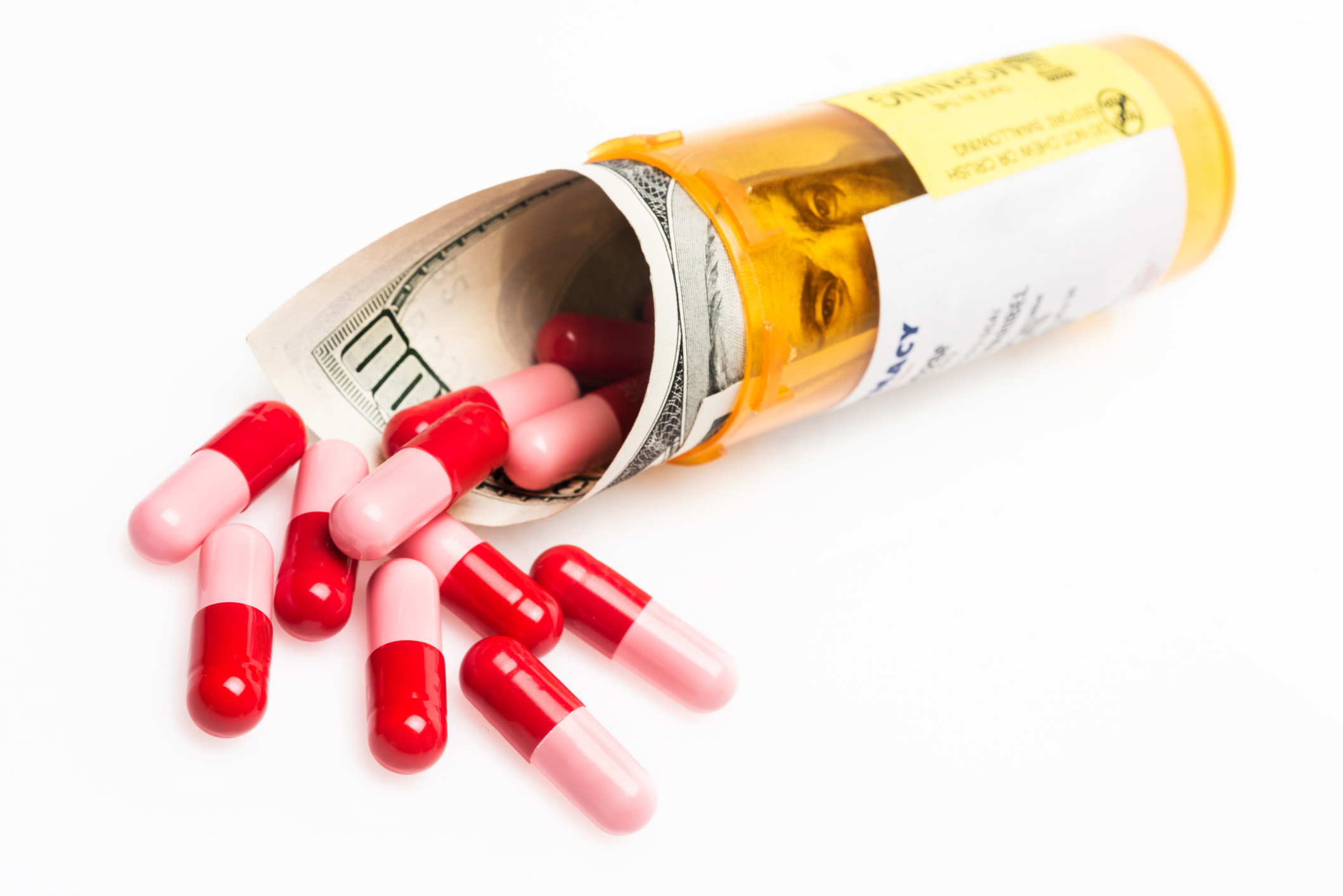 rolled 100 dollar bill inside a prescription drug container and pills on white background