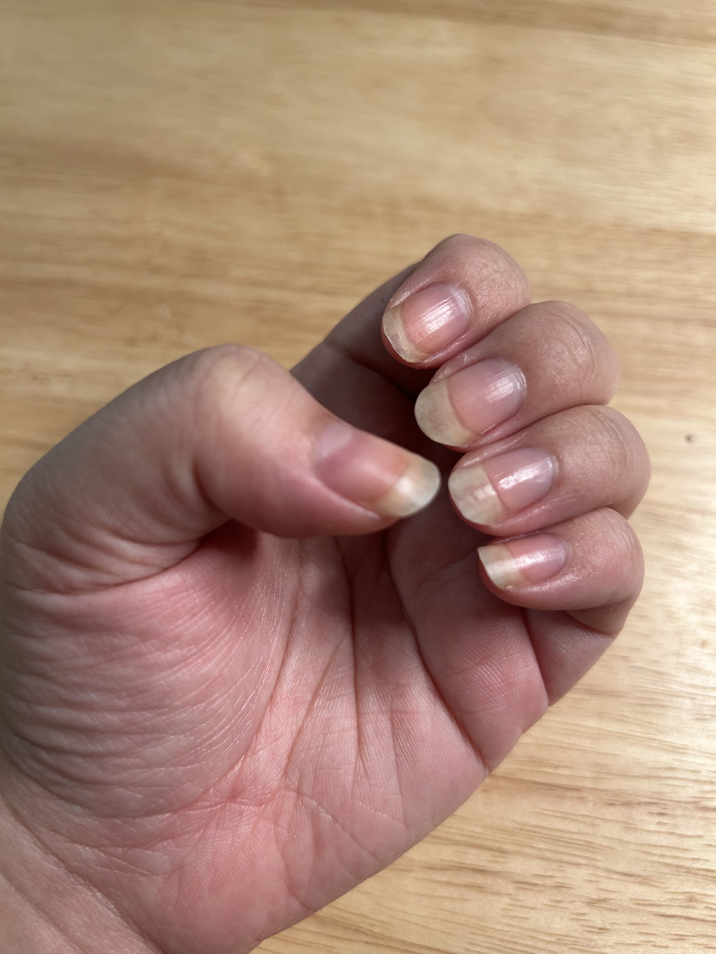 A woman's hand and nails before applying cuticle oil with a wood background.
