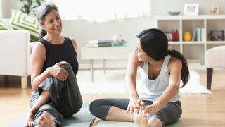 Two women sitting on yoga mats in living room, stretching to learn how to stop worrying