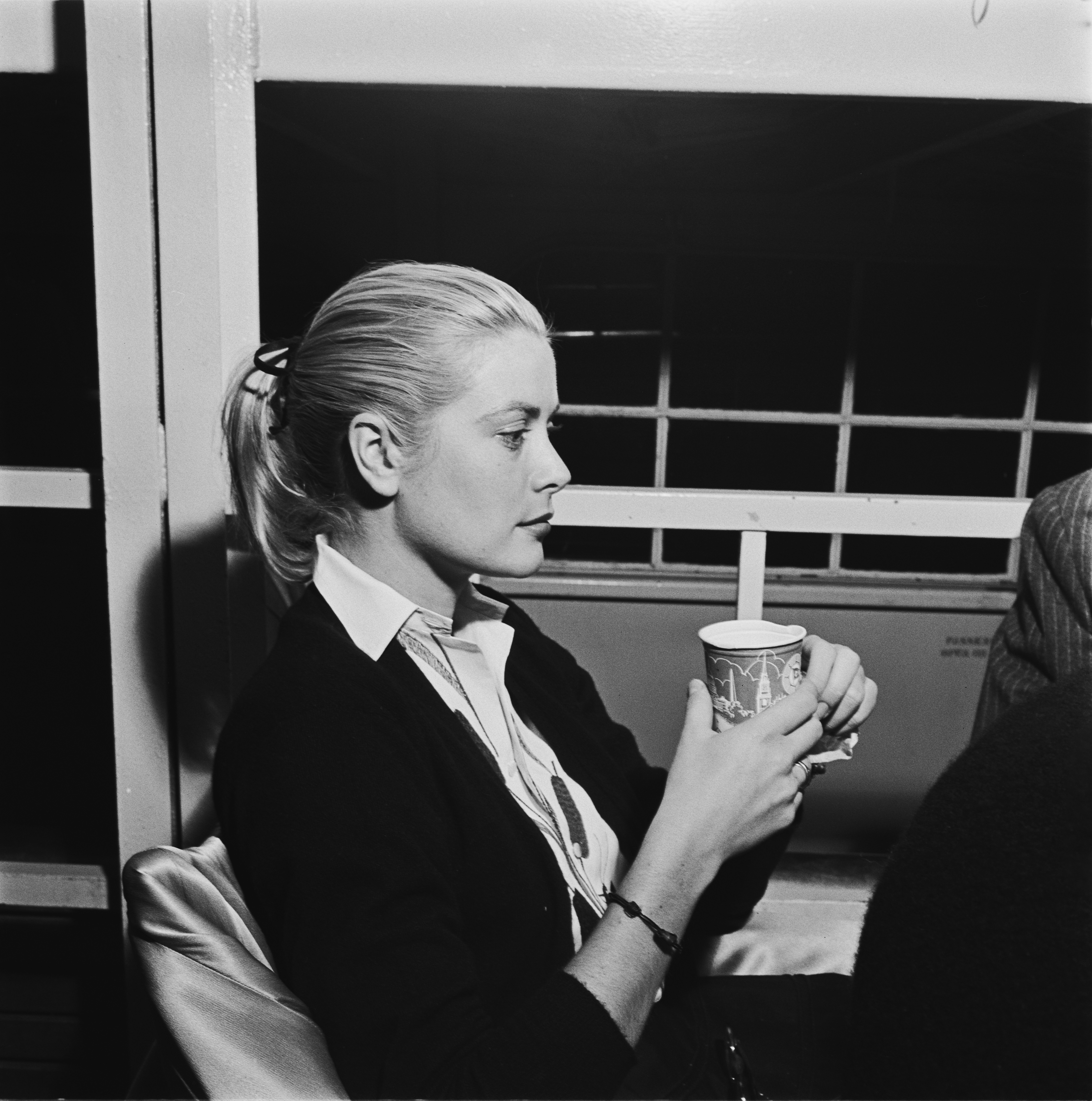 Princess Grace holding a paper cup sitting on a ferry