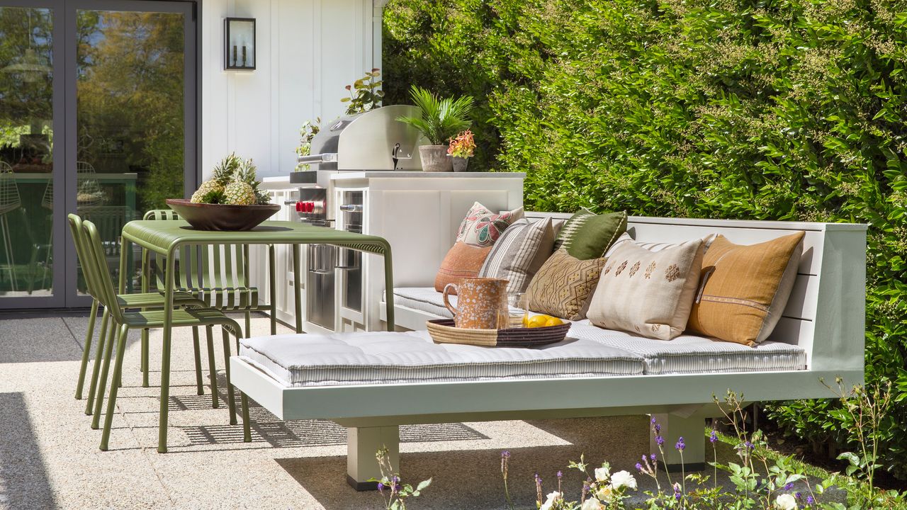 Outdoor patio with built-in kitchen and corner seating, and small green metal dining table and chairs set