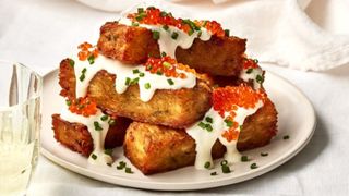 side shot of a stack of hash brown rectangles slathered in creme fraiche with chopped chives and trout roe