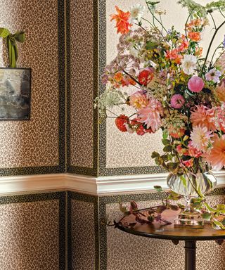 Leopard print wallpaper in brown and pink, wooden round table with vase of flowers