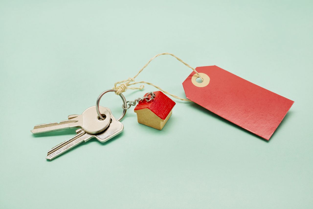 Still life of a keyring with keys, a small house and red price tag on turquoise colored background