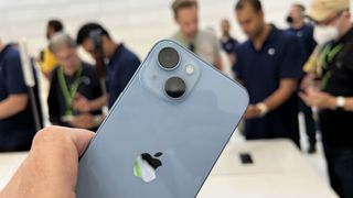 Nærbilde av baksiden til en blå Apple iPhone 14 som holdes opp under et pressearrangement.
