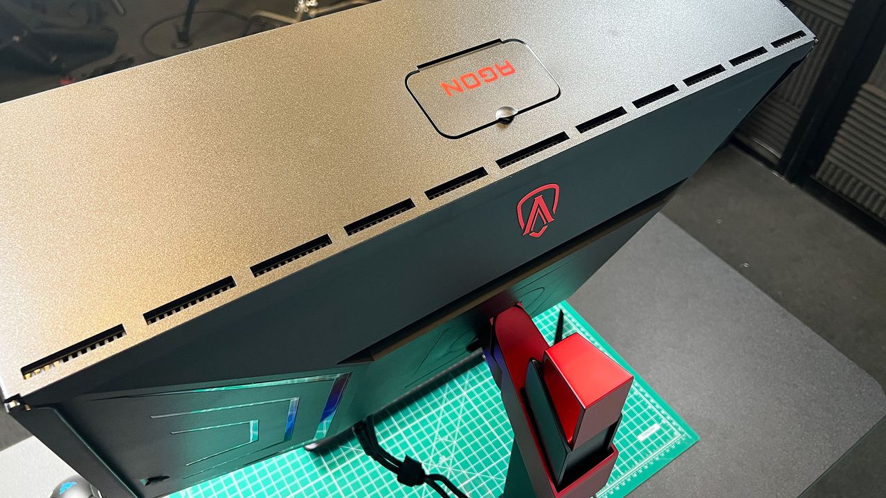 An AOC Agon Pro AG274QZM on a black desk with a green deskmat underneath