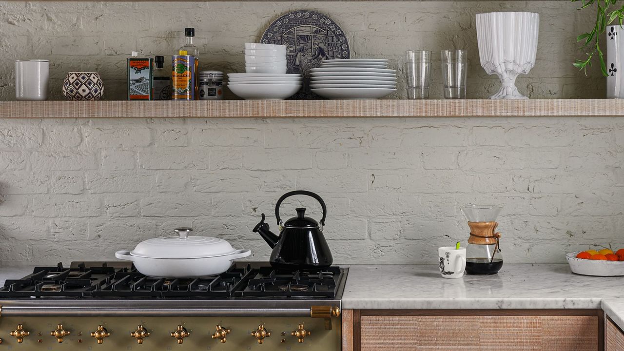 Modern kitchen range and fitted units with shelves and exposed painted brick wall and roof beams