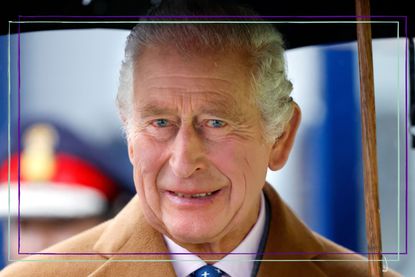 King Charles smiling stood under an umbrella