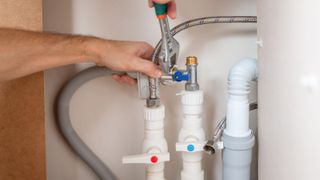 A man uses an adjustable wrench to install a water supply hose