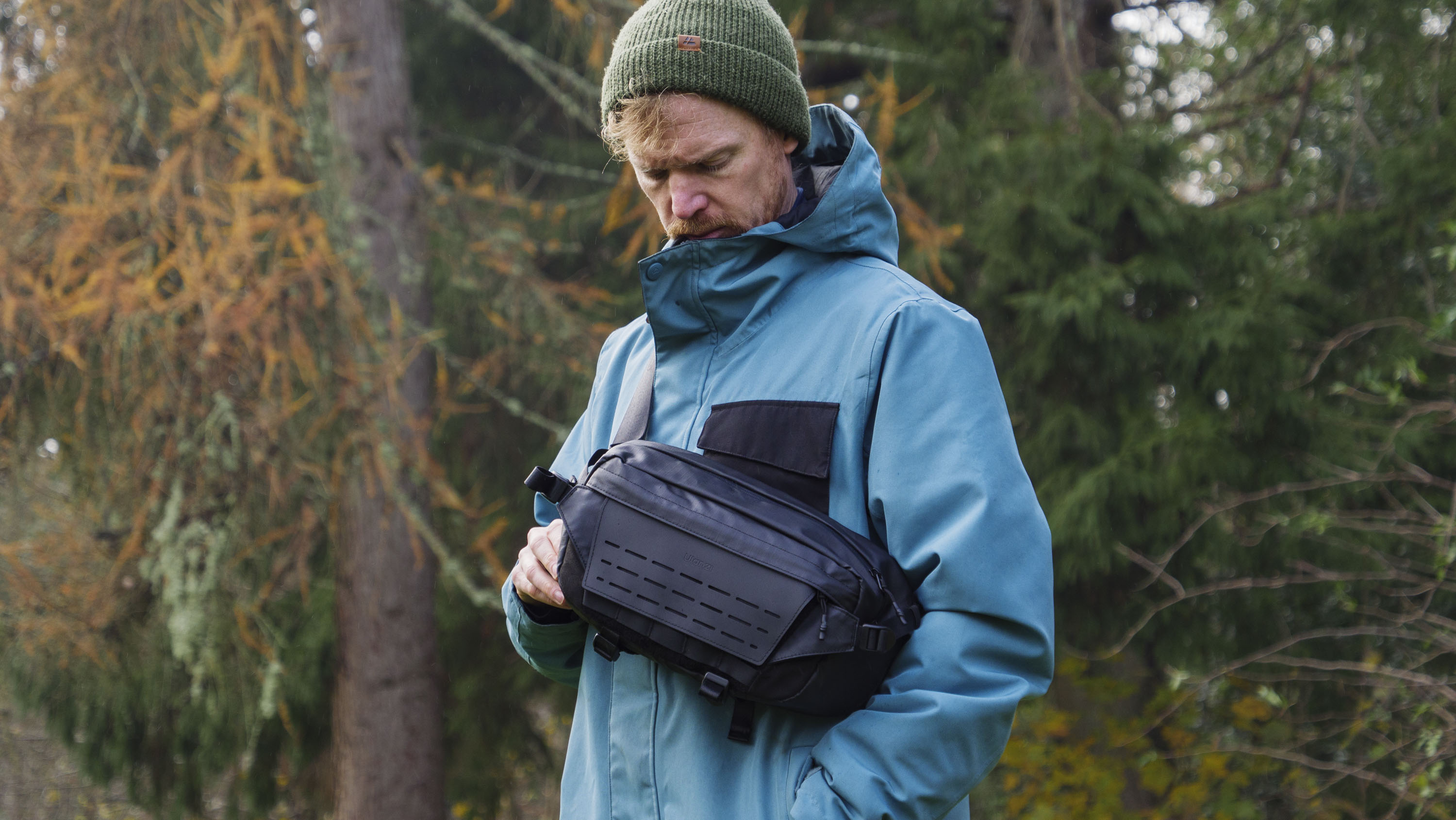Man wearing a blue jacket outside with a Ulanzi Camera Sling Bag over his shoulder and resting on his midriff