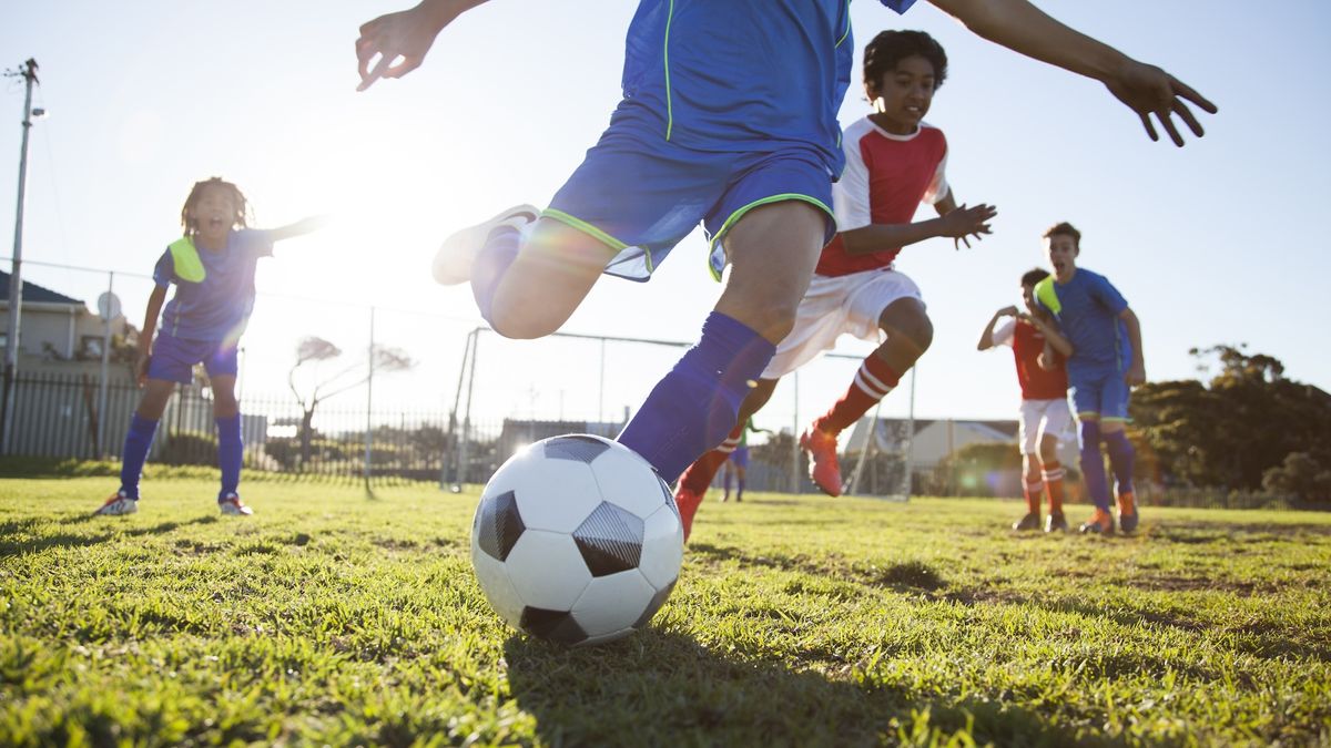 A group of young soccer players running to kick the ball on a field