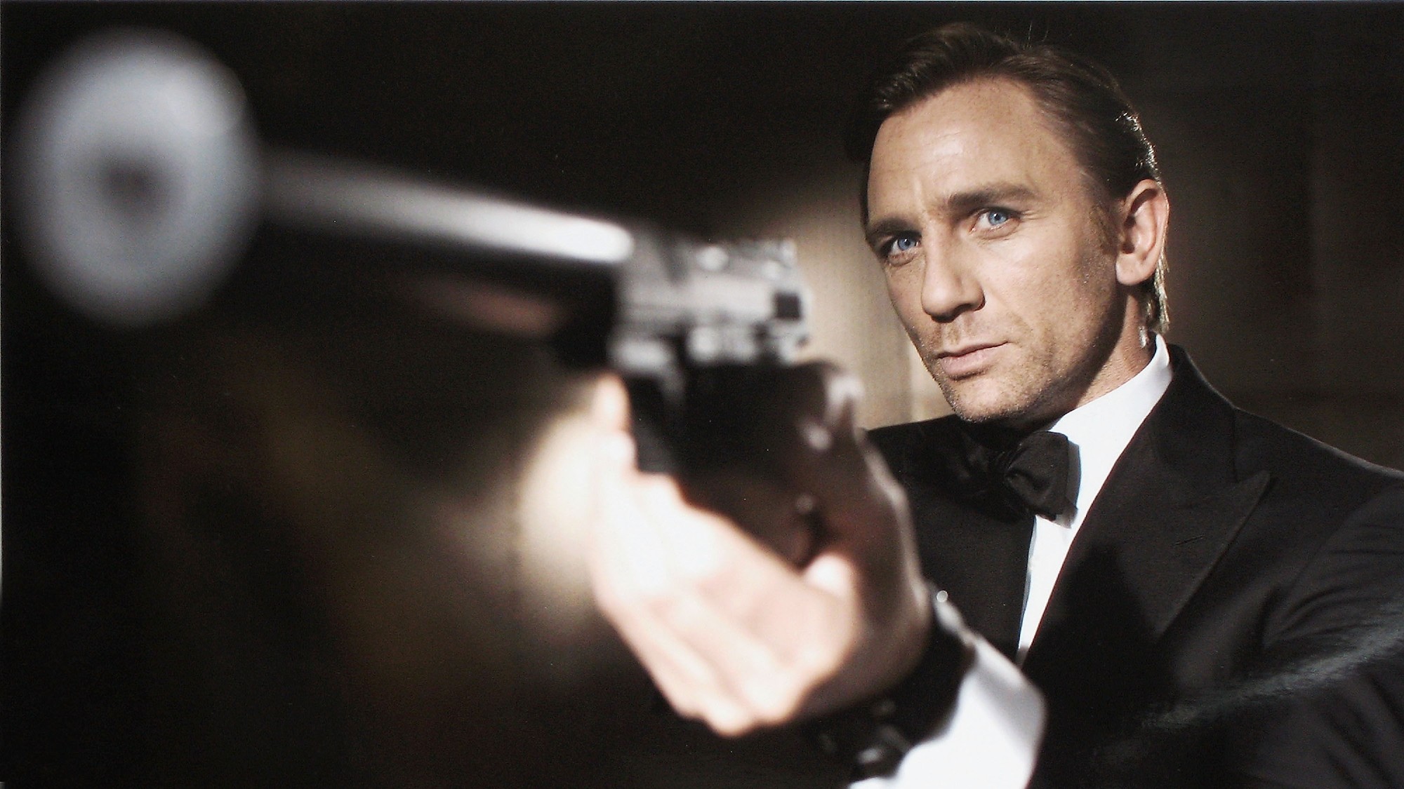 shot of Daniel Craig in his first Bond movie. he is dressed in a tuxedo and is pointing a gun to the side of the camera lens