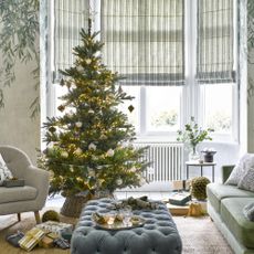 A living room with botanical-print wallpaper and a green sofa decorated for Christmas with a lit-up Christmas tree in the middle of the room