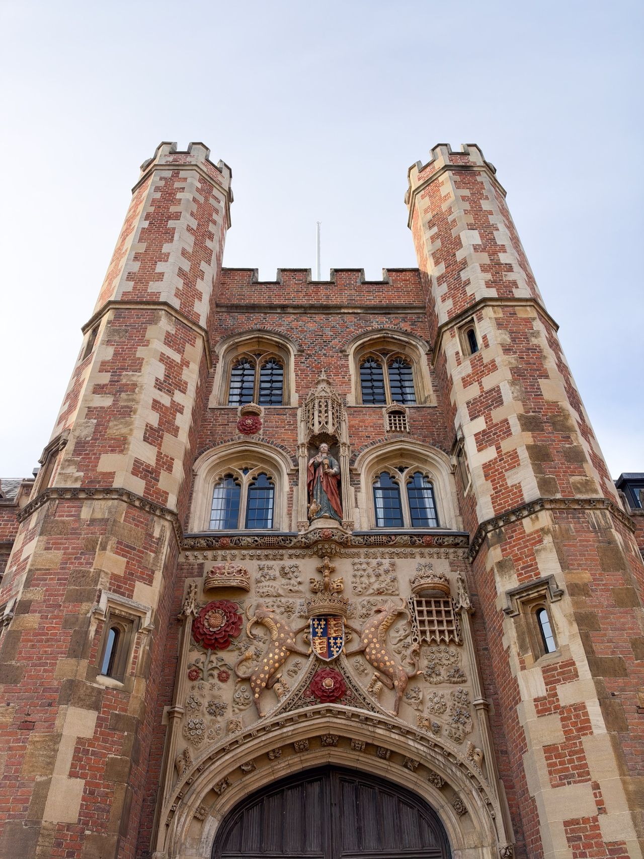 Low-angle view of an ornate red-brick gatehouse with twin towers, carved heraldic details, and a large arched doorway.