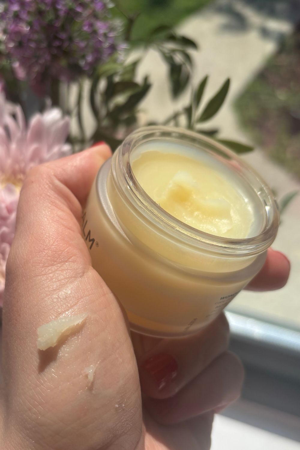 a hand holding a tub of wonderbalm with a smear of product