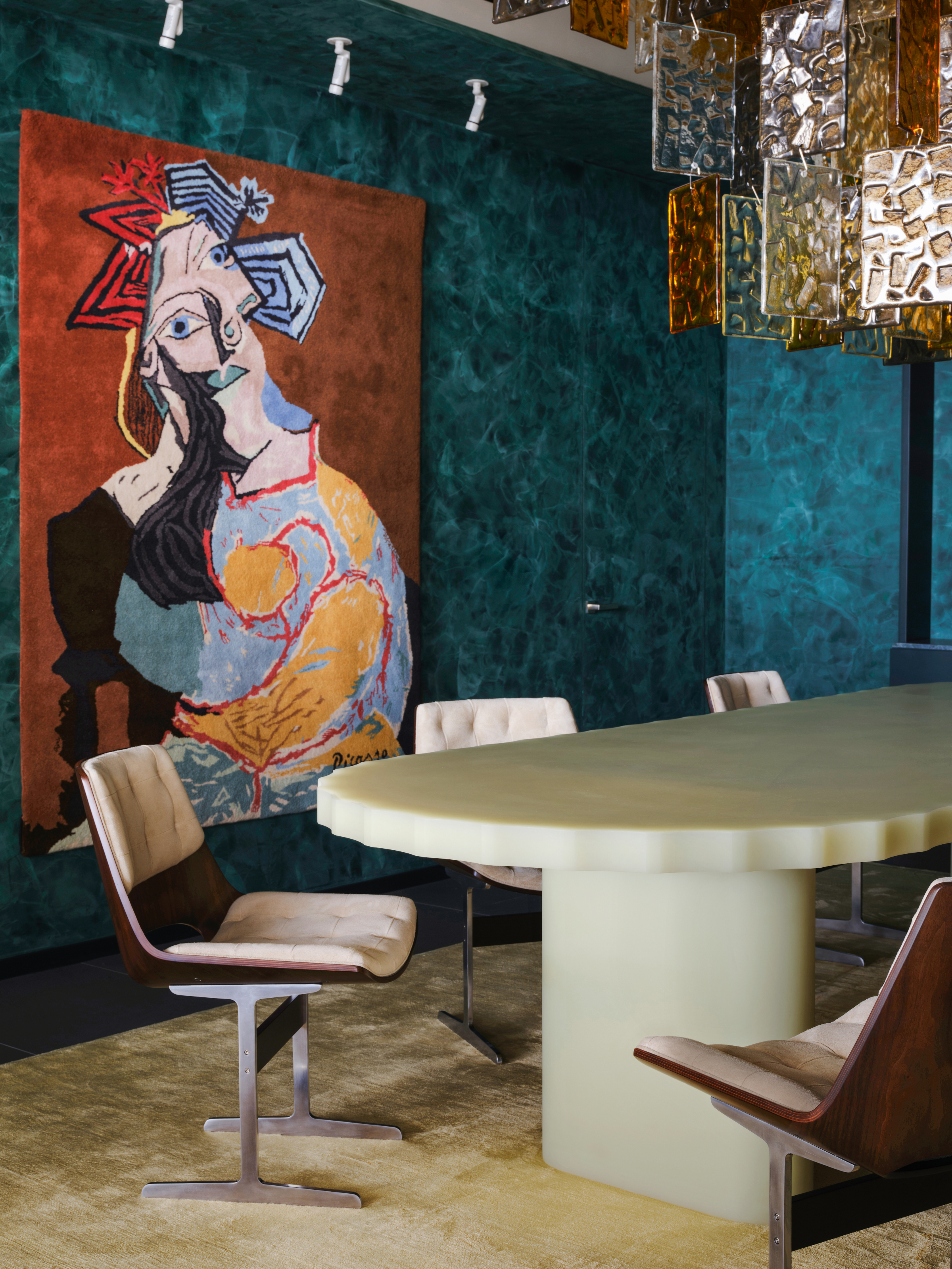 Dining room with forest green plaster walls, cast-glass chandelier, pale green resin table, custom yellow rug and artworks