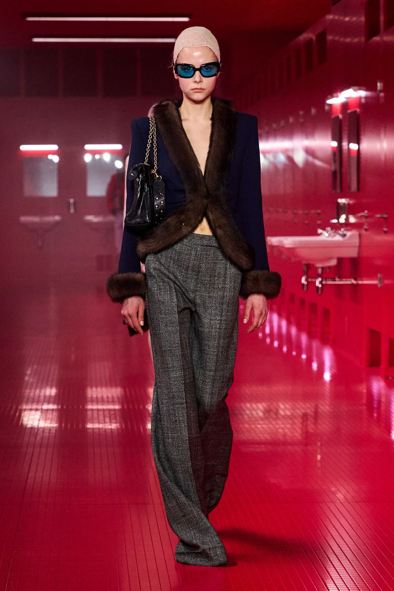 A model walking in the Valentino F/W 25 runway show wearing a cardigan with brown fur trim and gray trousers.