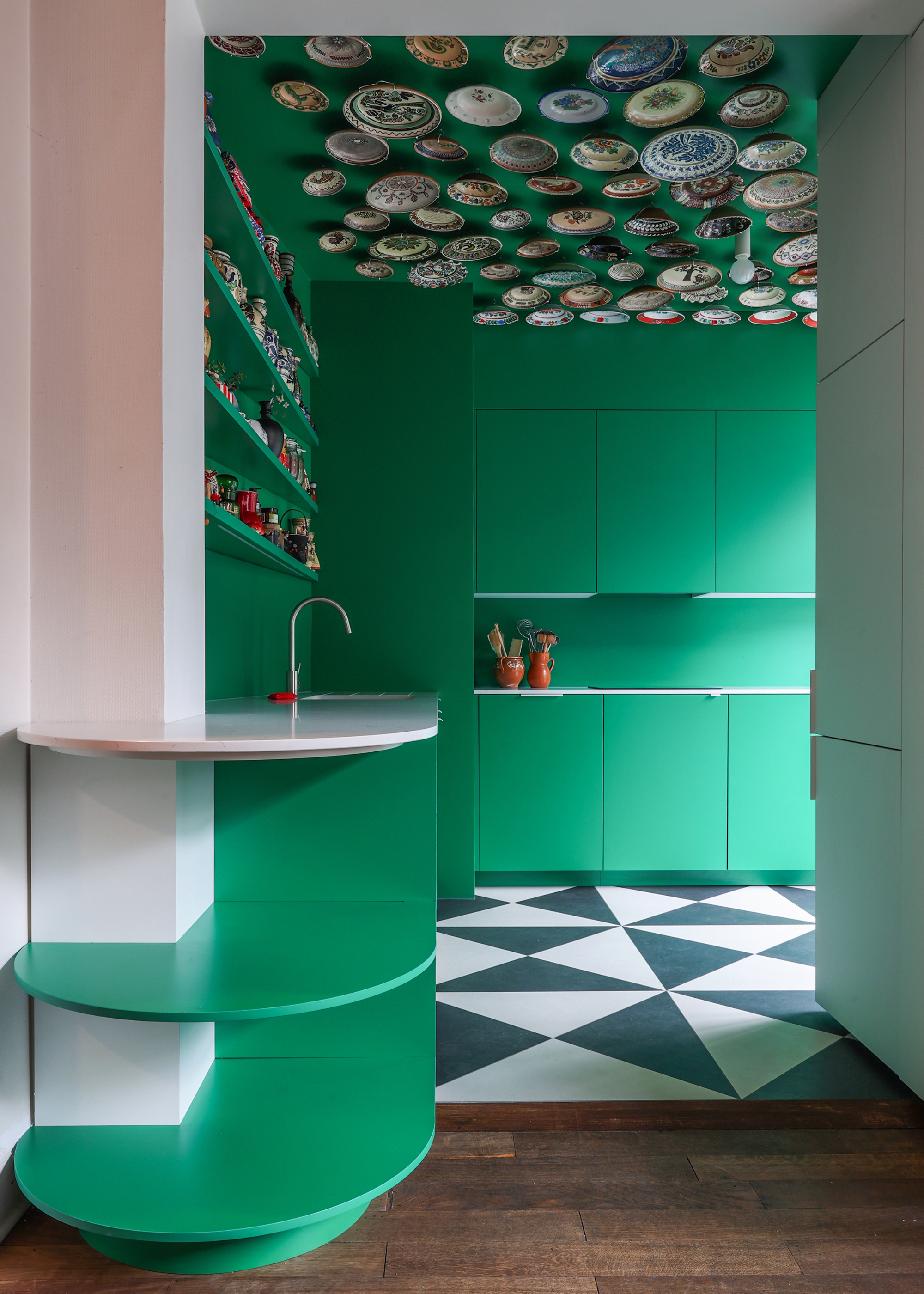 a look into a small kitchen color drenched in green, with black and white flooring and plates on the ceiling