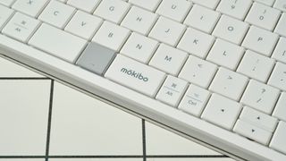 a closeup of the mokibo branded space bar on a white, lightweight tablet keyboard made by mokibo rests upon a white tiled table with a blue background