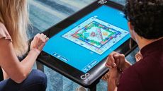 Infinity board game table in use by family playing Monopoly