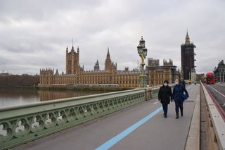 shot of Westminster bridge with river view and two people in face masks walking across the bridge