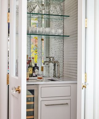 Built-in drinks area with mirrored backsplash, wine fridge, sink, prep area, and shelving for glassware.